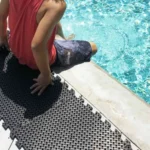 Person sitting on black drainage mats by a pool